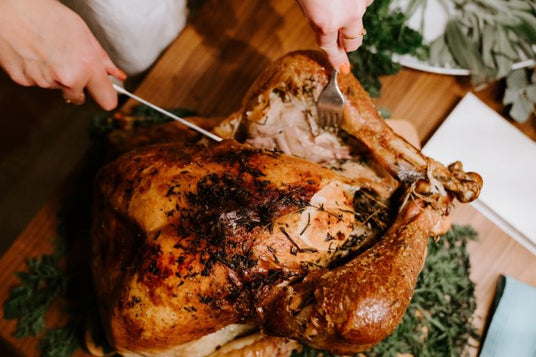Person carving a roasted turkey on a wooden cutting board with a festive background.